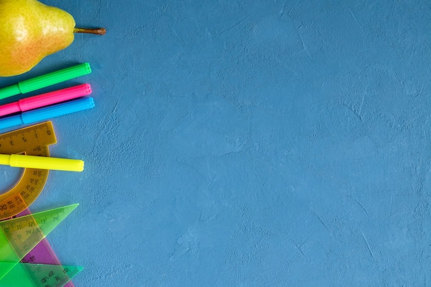 Photo fournitures scolaires et une poire sur fond bleu