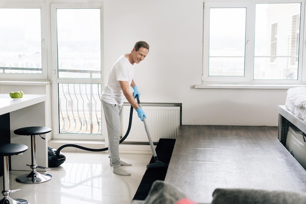 Foyer sélectif de l'homme heureux nettoyant l'appartement avec l'aspirateur