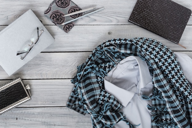 Fragment d'une chemise pour homme avec un keffieh sur un cintre, un journal intime, une bouteille d'eau sur une surface en bois peinte. Les couleurs pastel