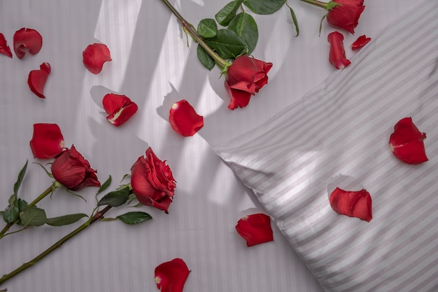 Un fragment de lit dans un hôtel ou à la maison avec décoration de roses rouges et pétales de draps blancs