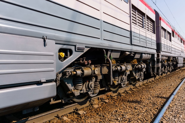 Fragment d'une locomotive moderne ensoleillée sur une voie avec des châssis de camion s'étendant en perspective