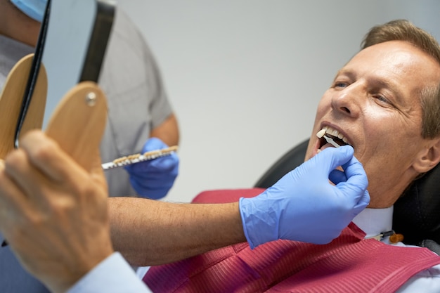 Photo fragment photo d'un homme d'âge moyen faisant un blanchiment des dents en clinique