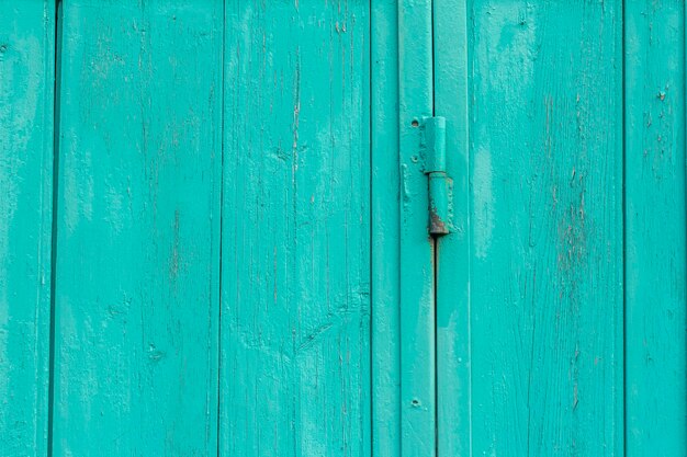 Un fragment d'une vieille porte en bois de couleur bleue ou turquoise sur des charnières rouillées.