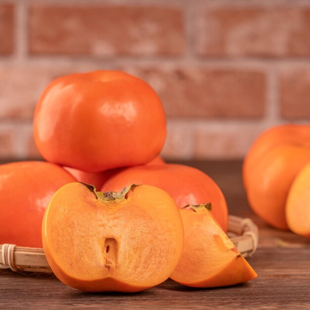 Frais beau kaki kaki sucré tranché sur une table en bois sombre avec fond de mur de brique rouge concept de design de fruits du nouvel an lunaire chinois gros plan