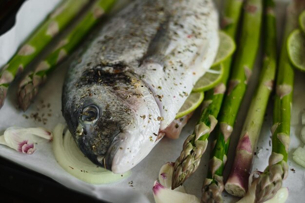 Frais éviscéré et assaisonné de sel et de sel prêt à cuire du poisson dorado sur une plaque à pâtisserie recouverte de papier sulfurisé avec asperges citron vert jeune ail et oignons