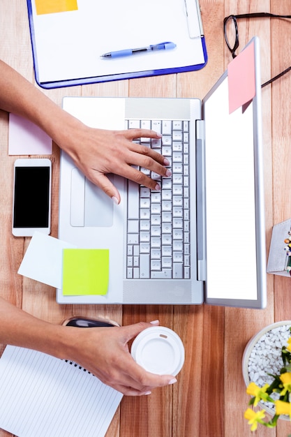 Frais généraux de mains féminines à l&#39;aide d&#39;ordinateur portable et tenant la tasse de café