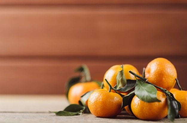 Photo frais petites mandarines juteuses avec des feuilles vertes dans un tas sur bois sombre