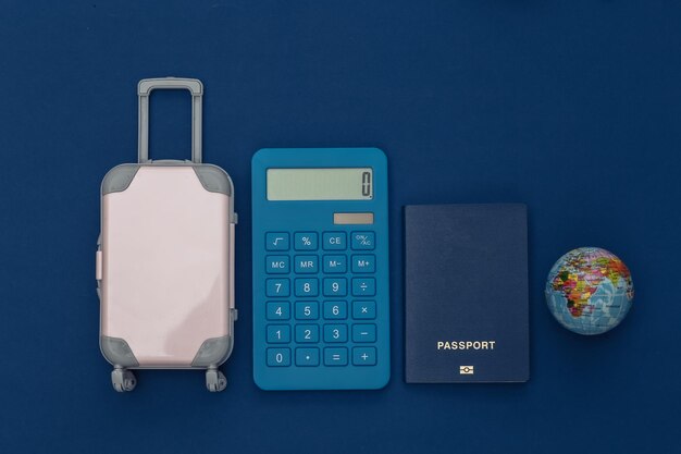 Frais de voyage. Mini valise de voyage en plastique avec calculatrice, passeport et globe sur fond bleu classique. Vue de dessus. Mise à plat