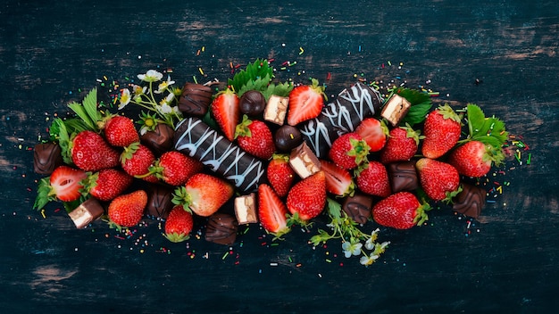 Fraise au chocolat et bonbons Sur un fond en bois noir Vue de dessus Copier l'espace