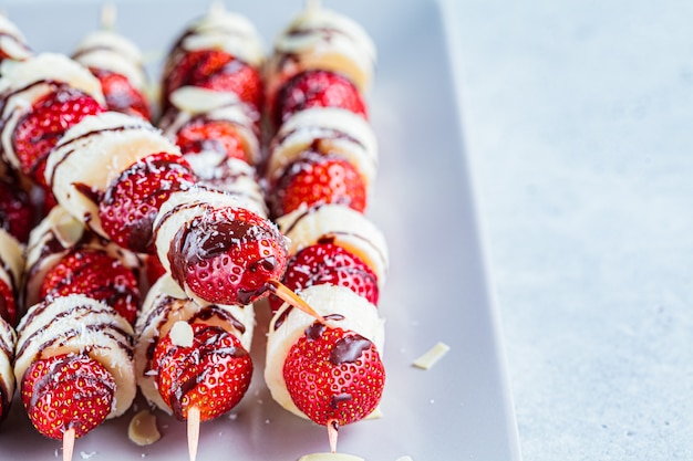 Fraise et banane au chocolat sur des brochettes. Désert d'été.