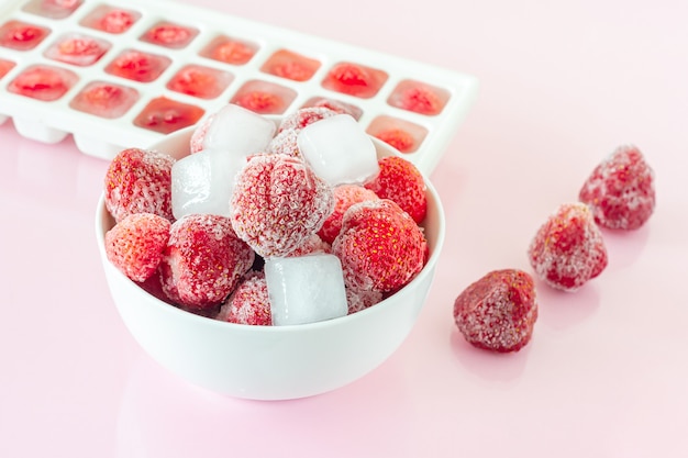 Fraise congelée avec des cristaux de glace sur fond rose.