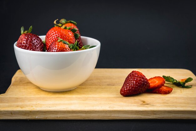 Une fraise coupée sur un bois et un bol blanc avec plus de fraises, recette de fraise maison