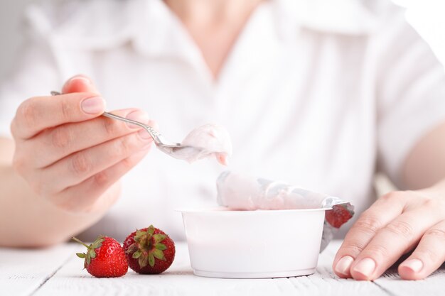 Fraise à la crème de lait sur un tableau blanc avec une cuillère à la main féminine