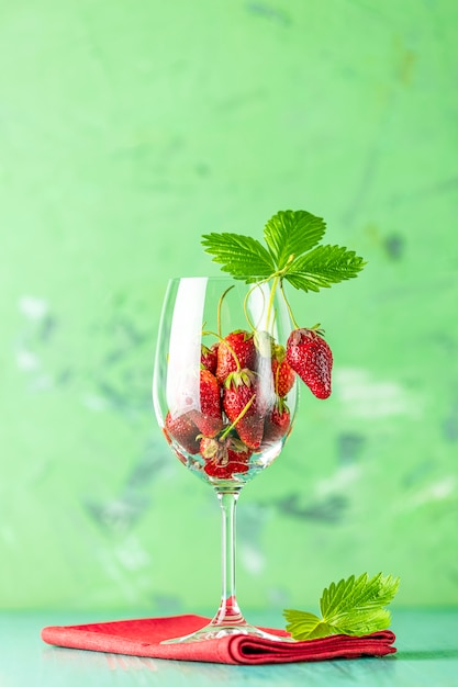 Fraise crue fraîche et mûre avec des feuilles vertes dans le verre à vin sur la surface verte.