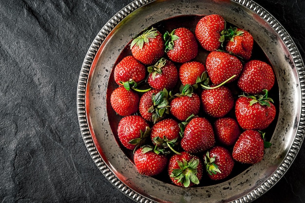 Fraise dans l'ancienne plaque de métal sur la vue de dessus de table en pierre noire