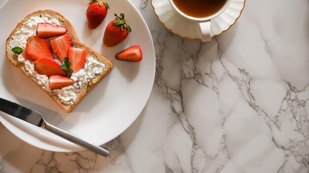 Fraise et fromage à la crème sur pain grillé à grains entiers servi avec thé anglais sur table en marbre