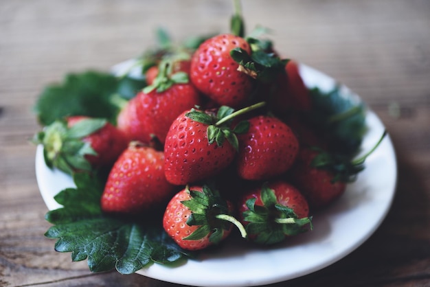 Fraise mûre rouge sur fond de plaque blanche, fraises fraîches sur la table en bois