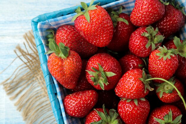 Fraise rouge dans un panier en osier avec du tissu bleu dessus sur une table en bois bleu clair.