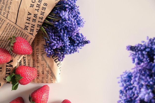 Fraise rouge fraîche et fleur de muscari pourpre avec un journal vintage sur fond blanc avec un espace de copie pour le texte