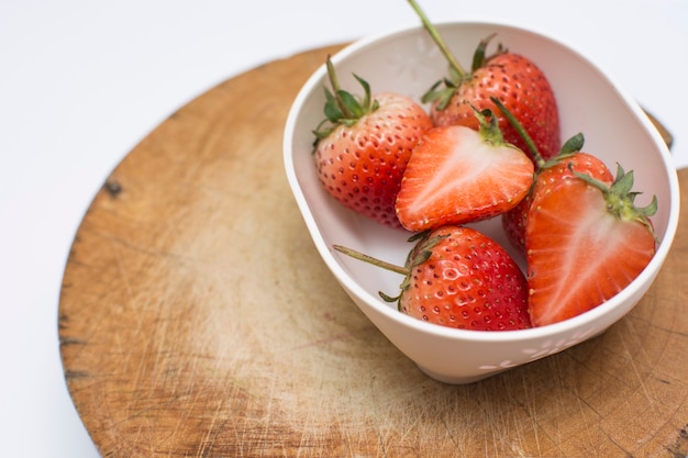 fraise tranchée dans un bol en céramique sur le bois à découper sur fond blanc.