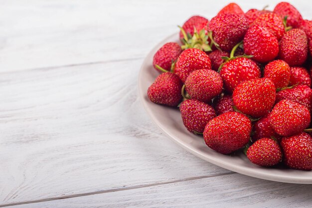 Fraises sur une assiette sur un fond en bois blanc