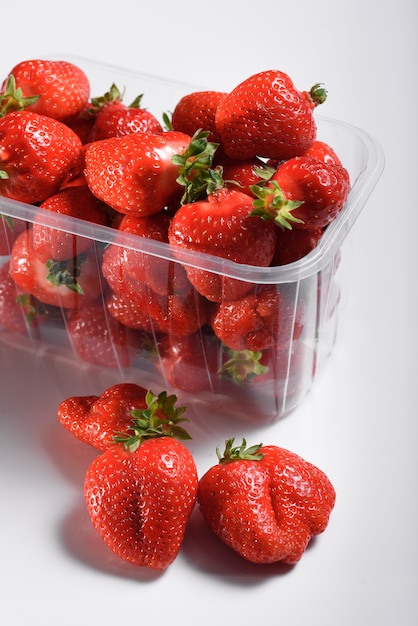 Fraises biologiques fraîches dans une boîte en plastique sur un mur blanc. livraison de produits biologiques. emballage de fraises biologiques.