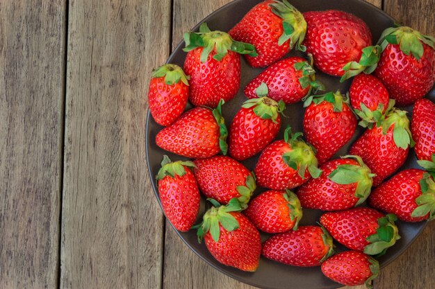 Fraises biologiques mûres sur une plaque noire sur fond de bois planche