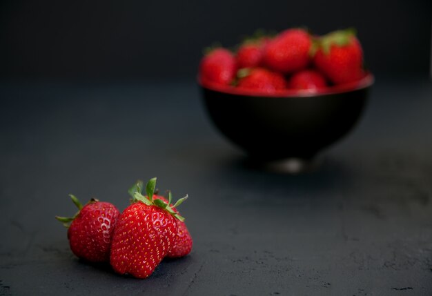 Fraises sur un bol noir et sur une surface noire