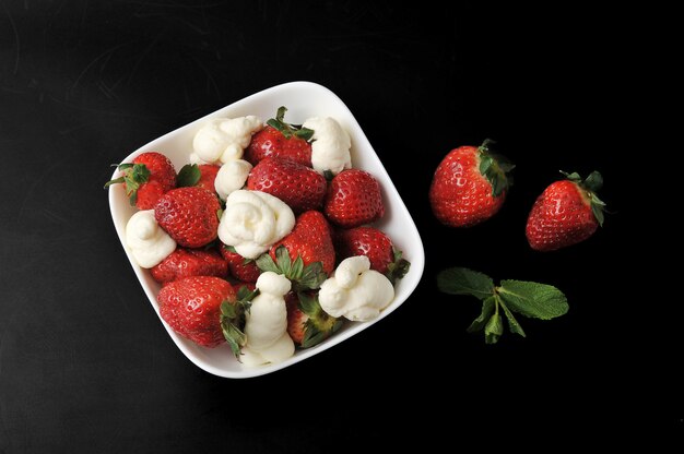 Fraises à la crème dans une assiette blanche sur une surface noire