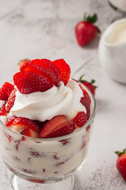 Des fraises avec de la crème dans une tasse en verre sur une table en ciment.
