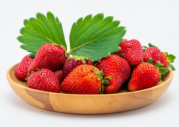 fraises dans une assiette en bois avec une feuille en gros plan sur fond blanc