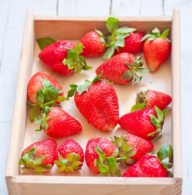 Des fraises dans une boîte en bois sur une table en bois blanc