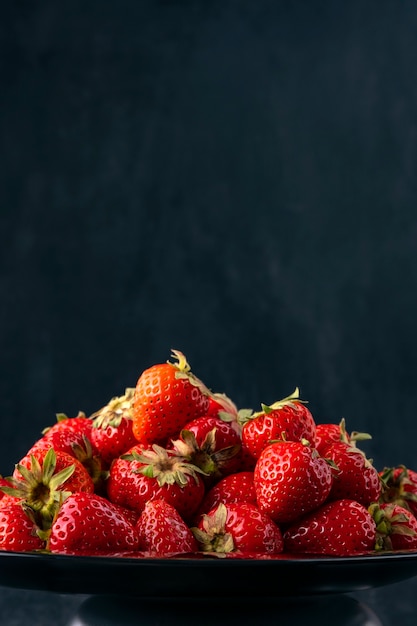 Fraises douces fraîches sur plaque sur fond noir, vue latérale. Fruits rouges, fruits de saison.