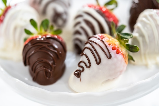 Fraises enrobées de chocolat blanc et noir sur un support à gâteau blanc.