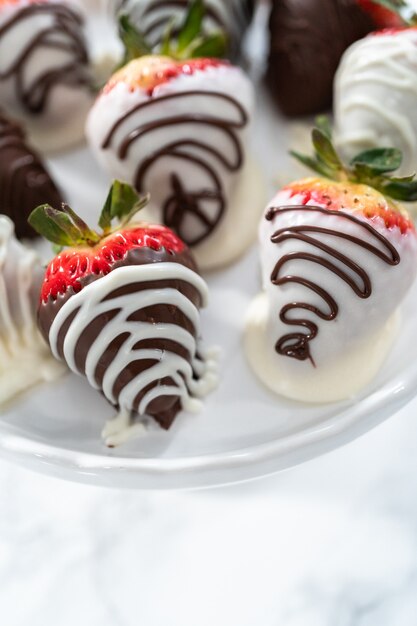 Photo fraises enrobées de chocolat blanc et noir sur un support à gâteau blanc.