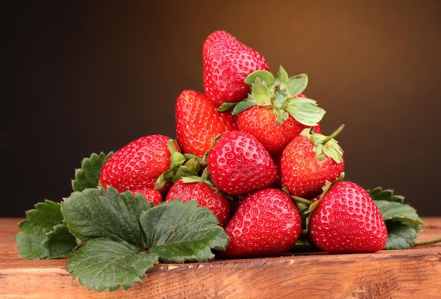 Fraises avec des feuilles sur une table en bois sur fond marron