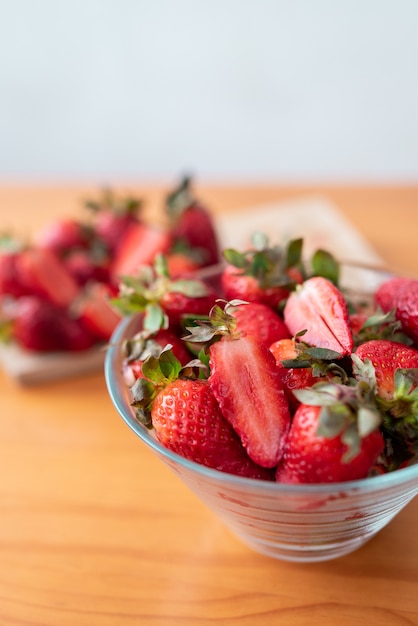 Fraises fraîchement coupées sur une planche à découper en bois et délicieuses fraises dans un bol en verre sur une table en bois.