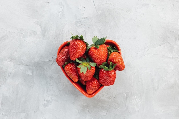 Fraises fraîchement cueillies dans un bol en forme de coeur sur fond gris rustique