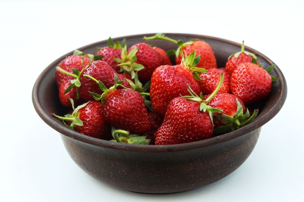 Fraises fraîches dans un bol brun sur fond blanc