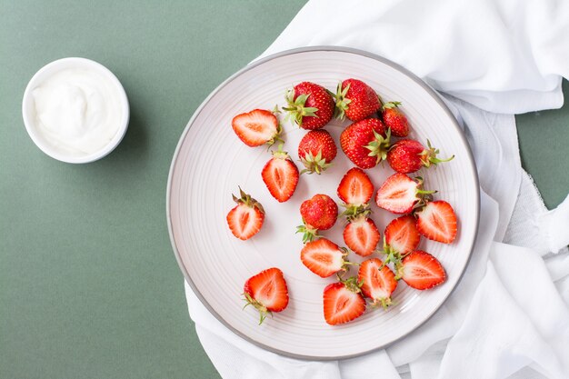 Fraises Fraîches Entières Et Tranchées Sur Une Assiette Et Crème Sure Dans Un Bol Sur Une Table Verte.