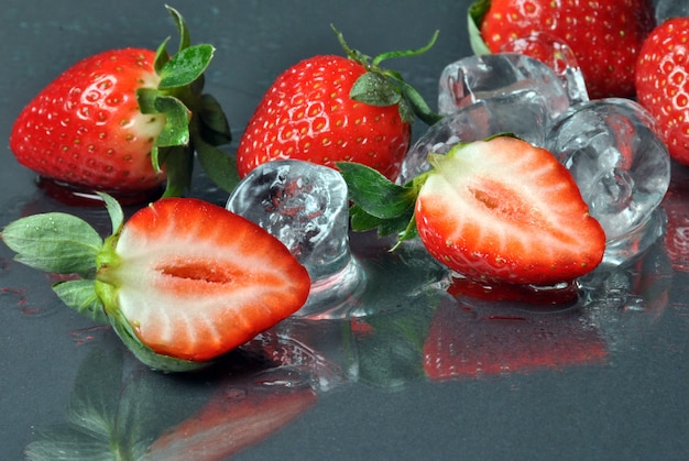 Fraises fraîches et glace sur fond noir avec reflet