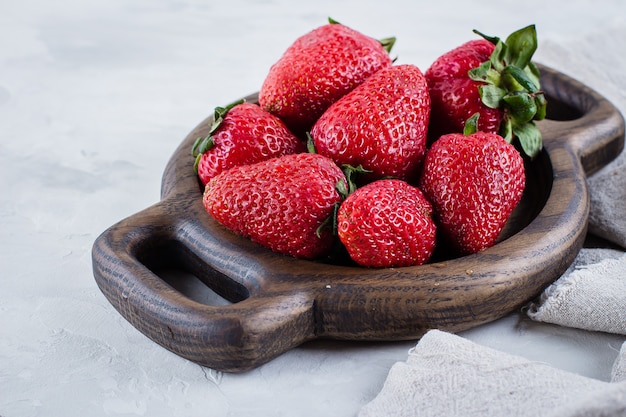 Fraises fraîches sur une plaque en bois sur fond de tableau blanc