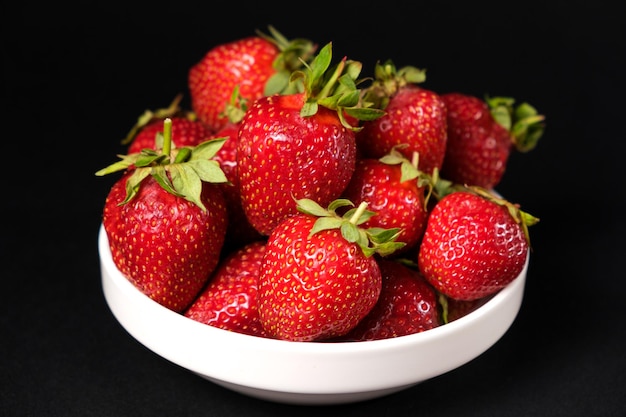 Fraises fraîches rouges dans une assiette blanche sur fond noir