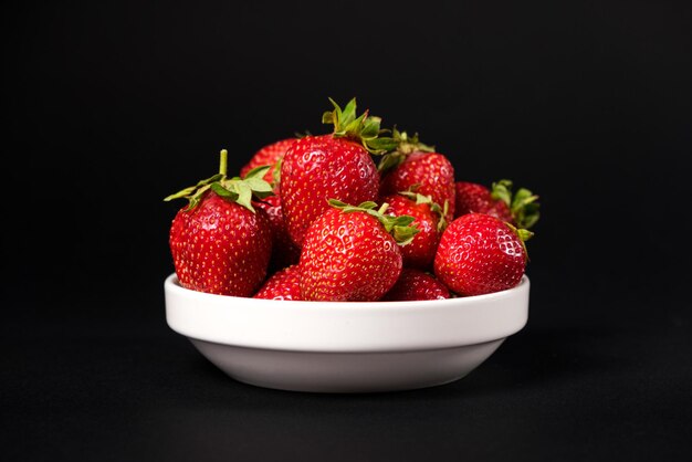 Fraises fraîches rouges dans une assiette blanche sur fond noir