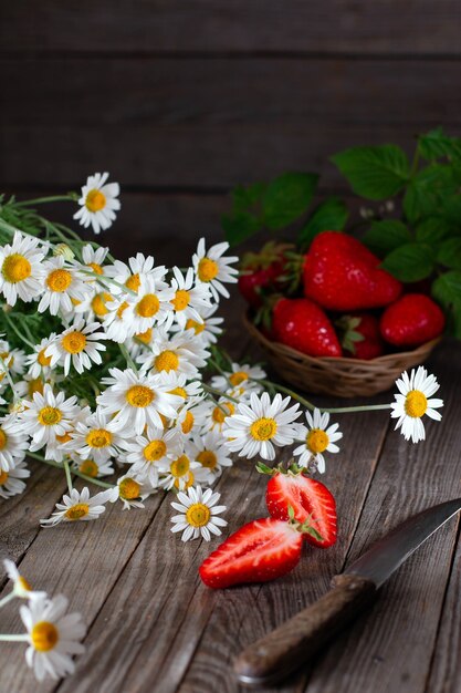 Fraises fraîches sur une table en bois avec un couteau et des fleurs de camomille d'été. Photo d'été