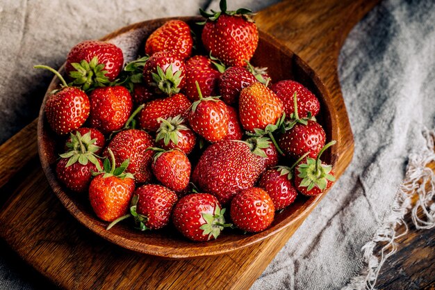 Fraises juteuses fraîches avec des feuilles sur un fond en bois