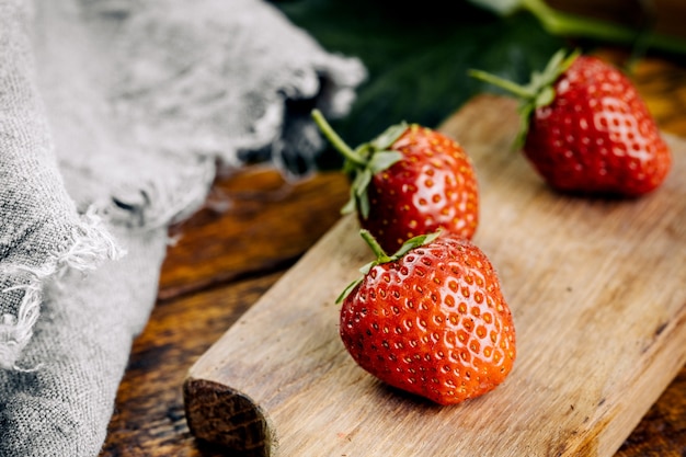 Fraises juteuses fraîches avec des feuilles sur un fond en bois.