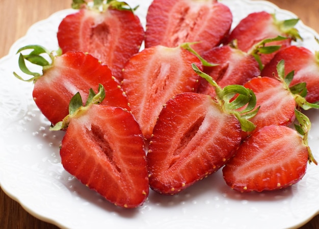 Fraises juteuses mûres coupées en deux sur une plaque blanche