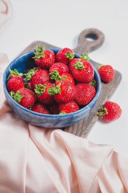 Fraises mûres dans un bol bleu sur planche de bois rustique, style élégant, baies sucrées pour le dessert d'été. Bol ou assiette rempli de fraises fraîches rouges. Récolte saisonnière. Fond de fraise élégant