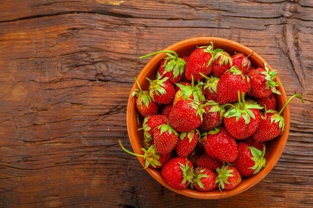 Fraises mûres dans une plaque d'argile sur une table en bois.